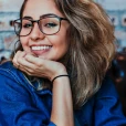 female with large eyeglassess smiling with her chin propped on her hand