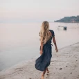 behind shot of woman walking on beach in a dress near the water