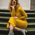 woman wearing a yellow knot dress with sunglassess while siting on steps and smiling