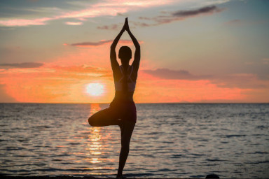 A woman meditating at dawn on a beach.