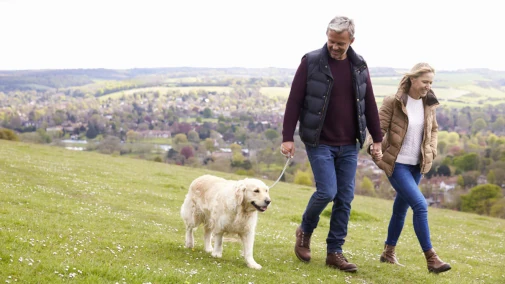 Happy couple walking their dog through a field.